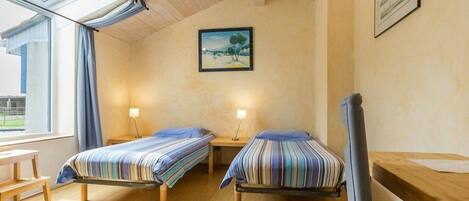 A room with two beds, wooden flooring, a skylight, and a painting on the wall.