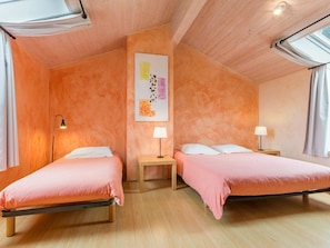 A room with two beds, wooden floors, a wall-mounted artwork, and a window with curtains.