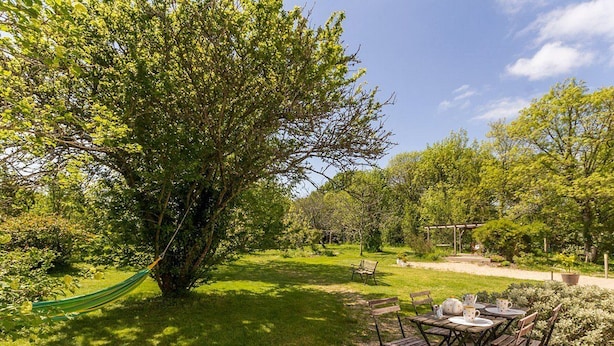 A garden with a hammock, a table with chairs, and a pergola.