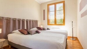 A bedroom with two beds, a window, a bedside table, and a floor lamp.