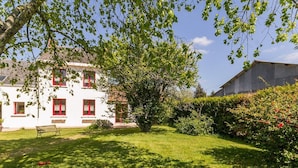 A white building with red window frames and a bench in the front yard.