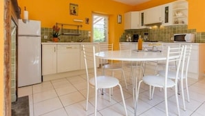 A bright kitchen with white cabinets, a white dining table with chairs, and a tiled floor.