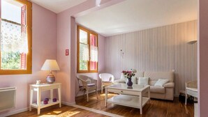 A living room with a white sofa, a coffee table, wicker chairs, a small white table with a lamp, and a radiator.