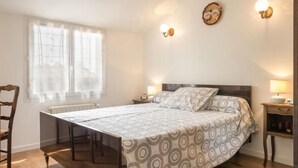 Ein Schlafzimmer mit einem Bett, einem Sessel, einem Tisch und einem Fenster mit Vorhängen.