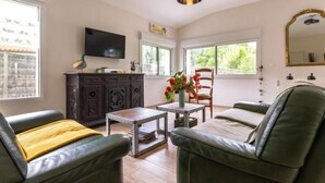 Un salon comprenant un téléviseur, un meuble en bois, une table ornée d’un vase de fleurs et deux canapés en cuir vert.