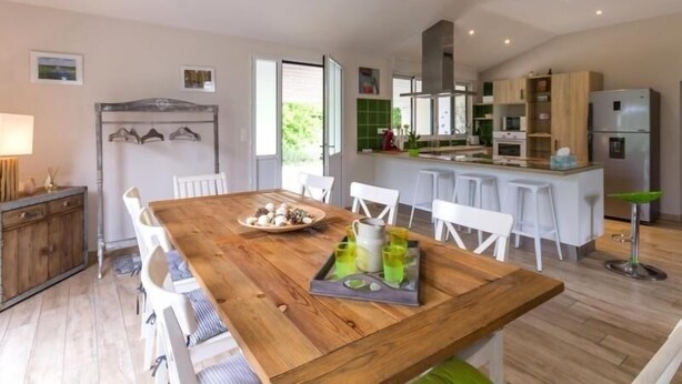 Une cuisine moderne avec une table à manger en bois, des chaises blanches et un coin bar avec des tabourets.
