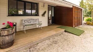 Une maison avec un porche en bois, un banc, un pot de fleurs et une porte de garage en bois.