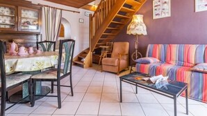 A cozy living room with a wooden staircase, a dining area with pink teapots, and a colorful striped sofa.