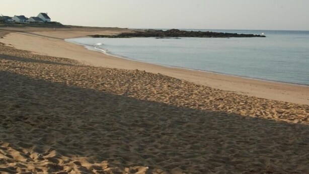 A beach with a sandy shore and a rocky outcrop in the water.
