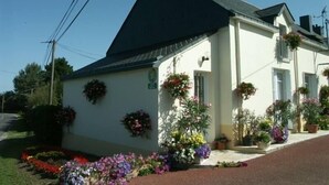 A white building with a black roof, surrounded by a variety of potted plants and flowers.