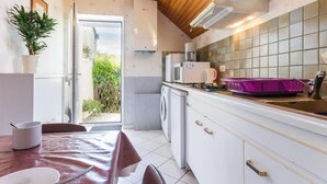 A compact kitchen with white cabinets, a microwave, and a sink. There's a dining area with a table and chairs, and a potted plant.