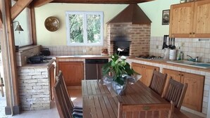 A rustic kitchen with a wooden table and chairs, a brick oven, and a stone wall. - Les chambres de Rocbaron (Rocbaron)