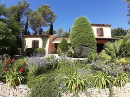 Uma villa com um jardim murado de pedra, uma árvore alta e um telhado de telhas.