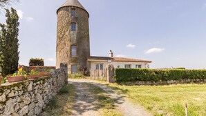 A stone tower attached to a building with a tiled roof, surrounded by a stone wall and a hedge.