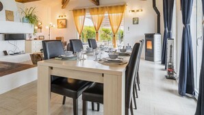 A dining area with a wooden table set for six, surrounded by chairs, with a fireplace and curtains in the background.