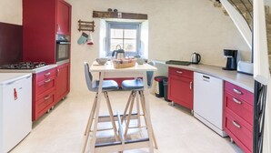 A modern kitchen with red cabinets, a white countertop, and a wooden stool. There is a window above the sink and a staircase to the right.