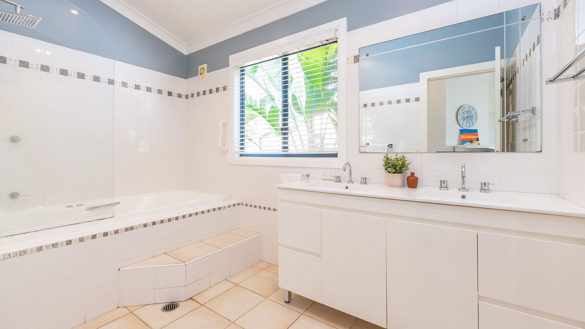 Ein modernes Badezimmer mit Badewanne, Waschbecken und einem Fenster mit Jalousien.
