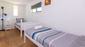 Una cama individual con una colcha a rayas, una mesita de noche con lámpara, una ventana con vistas y una lámpara de pie.