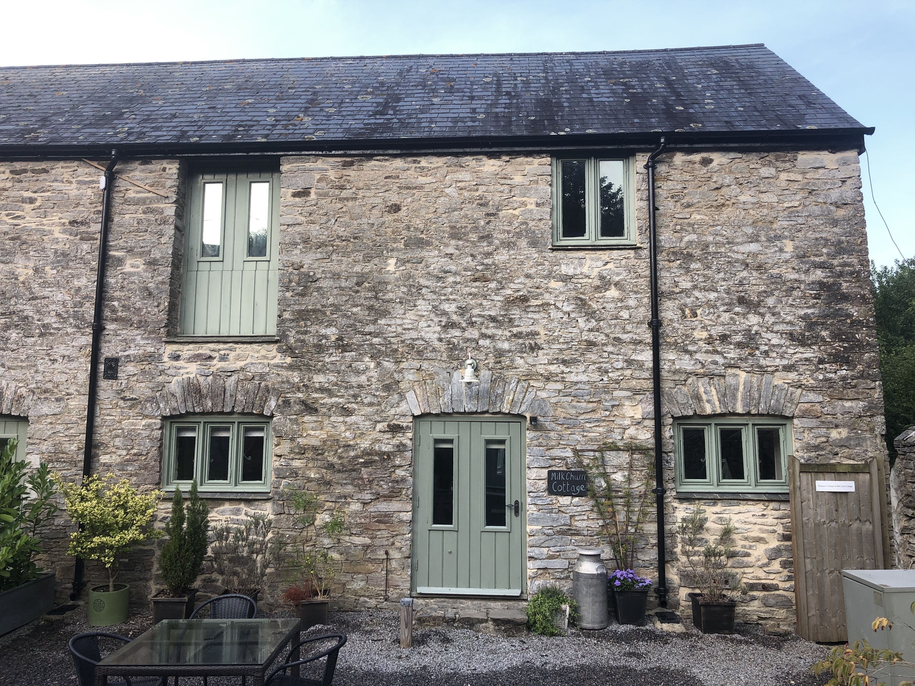 A stone cottage with a gravel patio, a glass table, and potted plants.