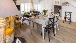 Ett rymligt vardagsrum med ett matbord för sex personer, omgivet av bekväma sittplatser. En trappa syns i bakgrunden och leder upp till en övre våning.