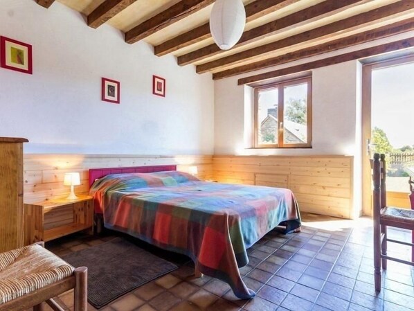 A bedroom with a bed, wooden headboard, bedside table, lamp, and a window with a view of the outside. - Stone House Retreat with Garden & WiFi in Tranquil Countryside (Moisdon-la-Rivière)