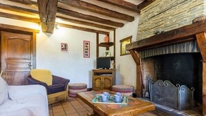 A cozy living room with a fireplace, wooden furniture, and a tiled floor. - Stone House Retreat with Garden & WiFi in Tranquil Countryside (Moisdon-la-Rivière)