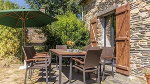 An outdoor patio with a stone building, wicker chairs, a wooden table, and a green umbrella. - Stone House Retreat with Garden & WiFi in Tranquil Countryside (Moisdon-la-Rivière)