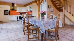 Un coin repas avec une table dressée pour quatre personnes, entourée de chaises en bois. Un vase rempli de fleurs est posé sur la table.
