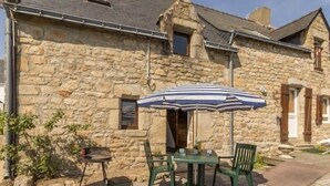 A stone building with a patio area featuring a table and chairs, an umbrella, and a grill.