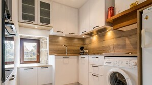 A modern kitchen with white cabinetry, a built-in washing machine, and a window with a stone wall view.