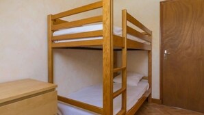 A bunk bed with three levels, a wooden wardrobe, and a wooden door.