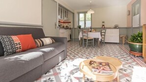 En kompakt opholdsstue med sofa, spisebord og et tekøkken.