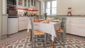 Et køkken med spisebord dækket til to personer, samt et køleskab, en mikrobølgeovn og en blender på bordet.