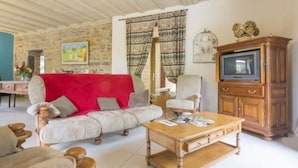 Una sala de estar acogedora con un sofá rojo, una mesa de centro de madera, un televisor y una pared de piedra.
