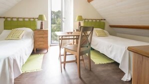 Una habitación pequeña y acogedora con dos camas, una mesa de madera y una silla.