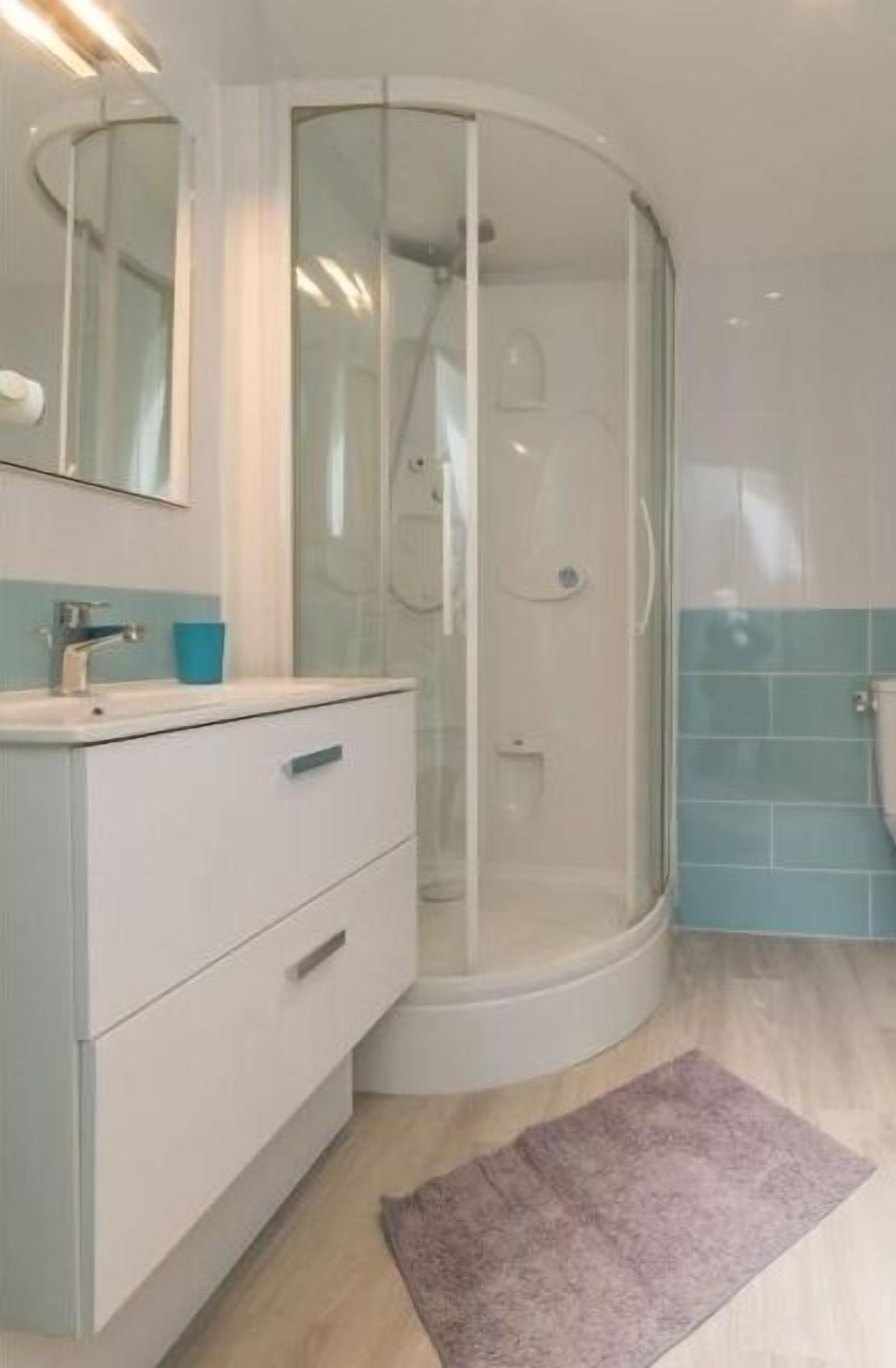 Un baño con ducha envuelta en vidrio, tocador blanco con cajones y pared revestida con azulejos azules.
