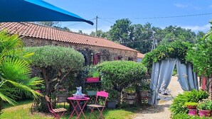 A rustic stone building with a tiled roof, a gravel path, and outdoor seating with a table and chairs. - Seaside Eco Cottage: 18th-Century Stone House near Pornic, 15min to Beach, Accessible, Private Garden (Arthon-en-Retz)