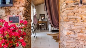 A stone-walled hallway leading to a room with a bed, a desk, and a chair. - Seaside Eco Cottage: 18th-Century Stone House near Pornic, 15min to Beach, Accessible, Private Garden (Arthon-en-Retz)