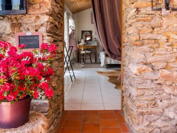 A stone-walled hallway leading to a room with a bed, a desk, and a chair.