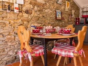 A stone-walled dining area with a round wooden table set for four, featuring plaid tablecloths and red polka-dotted bowls.