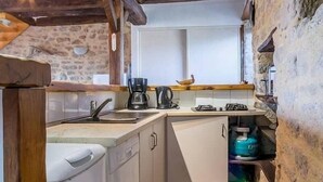 A compact kitchen with a stone wall, wooden beams, a washing machine, a coffee maker, and a water dispenser. - Charming Cottage Near Salt Marshes & Guérande Walls with Enclosed Garden and Terrace (Guérande)