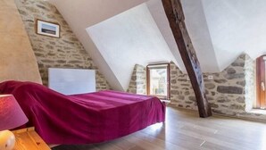 A bedroom with a sloped ceiling, stone walls, a bed with a pink bedspread, and a wooden nightstand. - Charming Cottage Near Salt Marshes & Guérande Walls with Enclosed Garden and Terrace (Guérande)