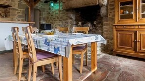 A rustic dining area with a stone wall, wooden beams, and a table set for four. - Charming Cottage Near Salt Marshes & Guérande Walls with Enclosed Garden and Terrace (Guérande)
