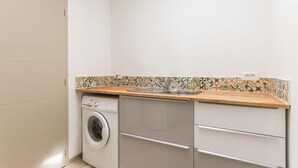 Une cuisine de taille réduite, équipée d’un lave-linge, d’un évier et d’un pare-feu en carrelage.
