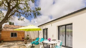 Une terrasse avec une table et des chaises, un parasol jaune et un bâtiment en bois en arrière-plan.