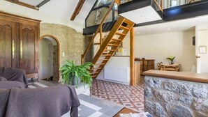 Un vaste espace de vie doté d’un plafond haut, de poutres apparentes, d’un mur en pierre et d’un escalier menant à un niveau supérieur.