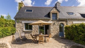 Une maison en pierre avec un patio, une table entourée de chaises et un parasol.