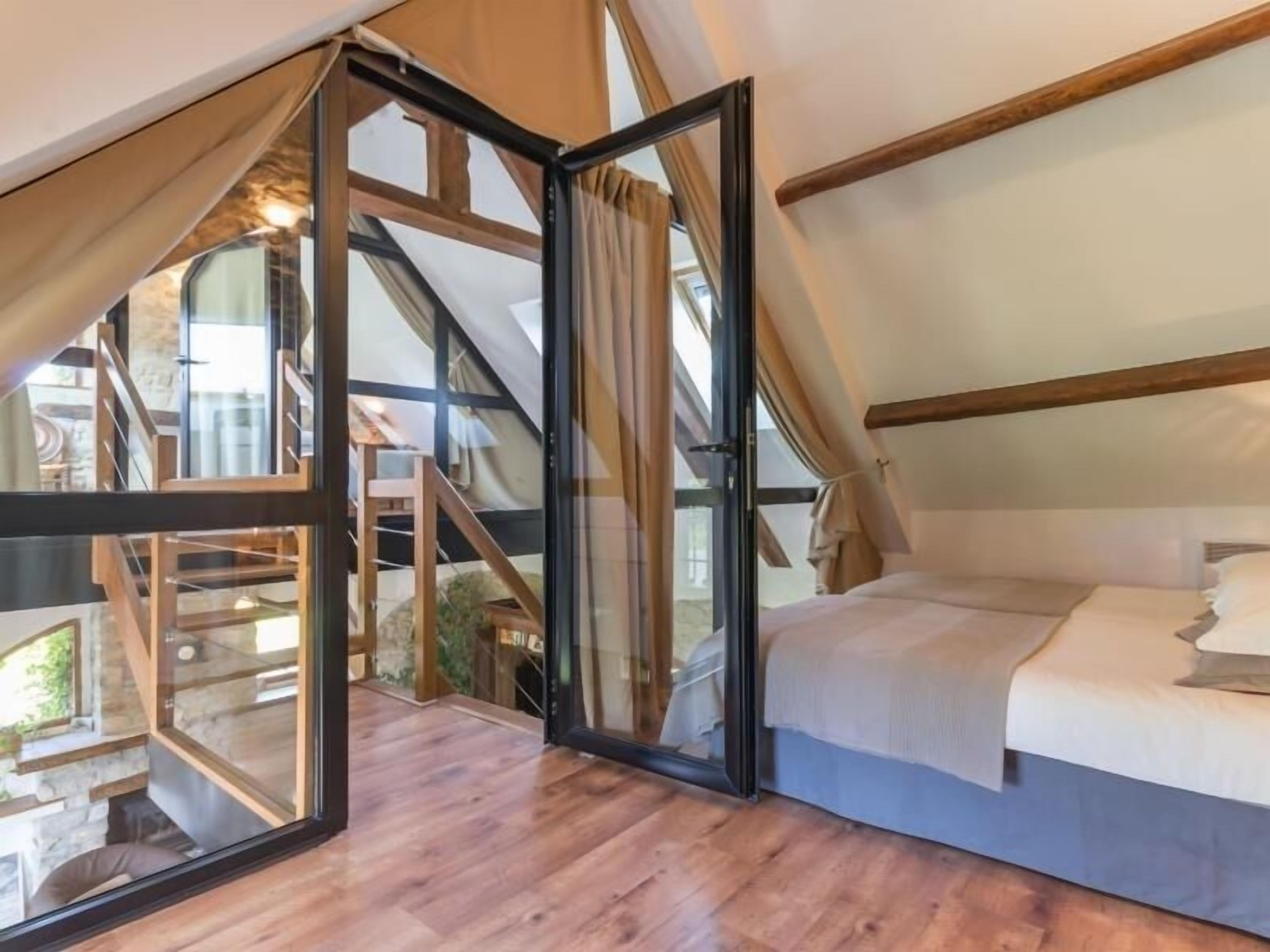 Un dormitorio con un ventanal grande, suelo de madera y una cama con ropa de cama blanca.