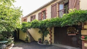 A building with a yellow facade, wooden shutters, and a dark brown gate. There is a staircase leading to a second floor, and potted plants are visible. - Charming Renovated Farmhouse with Pond, Near Nantes - WiFi, Baby Equipment Included (Corcoué-sur-Logne)