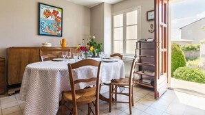 Un coin repas avec une table dressée pour quatre personnes, des chaises, un buffet en bois et un tableau accroché au mur.